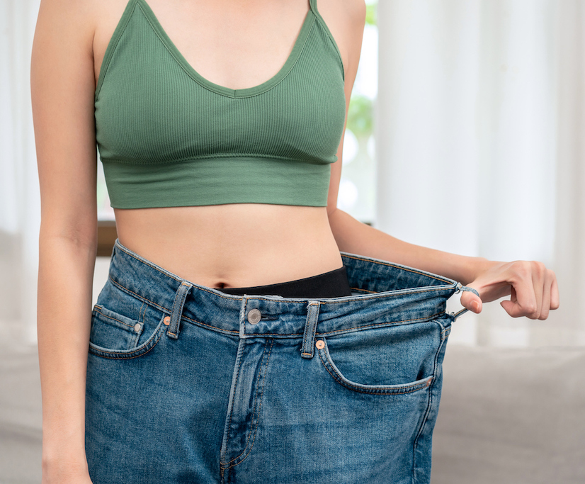 Sporty woman is smiling while wearing in loose big jean to showing successfully of weight loss