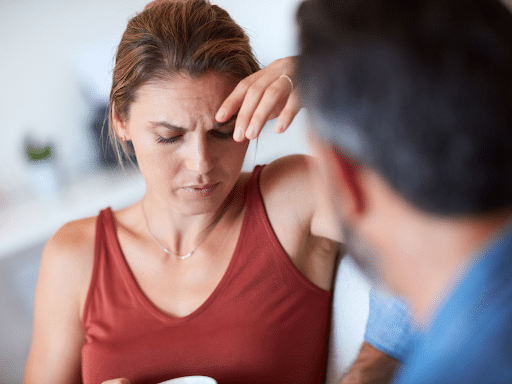 Woman touching her forehead and looking distressed while talking to someone, showing possible fatigue or emotional stress.