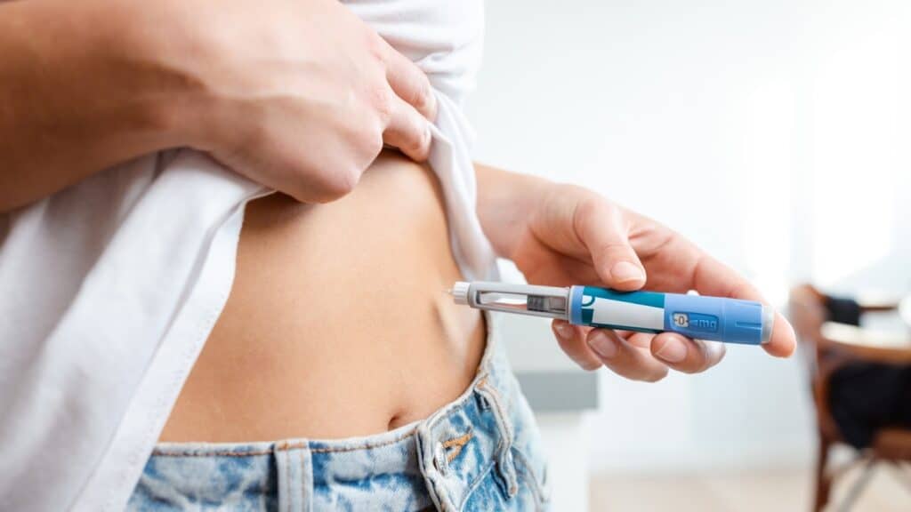 A close-up of a patient administering a subcutaneous lose weight injection into the abdomen using a pre-filled medication pen.