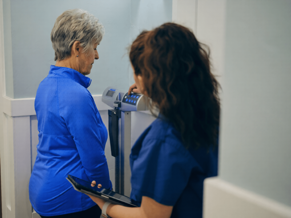 A clinician is helping a woman check her weight.
