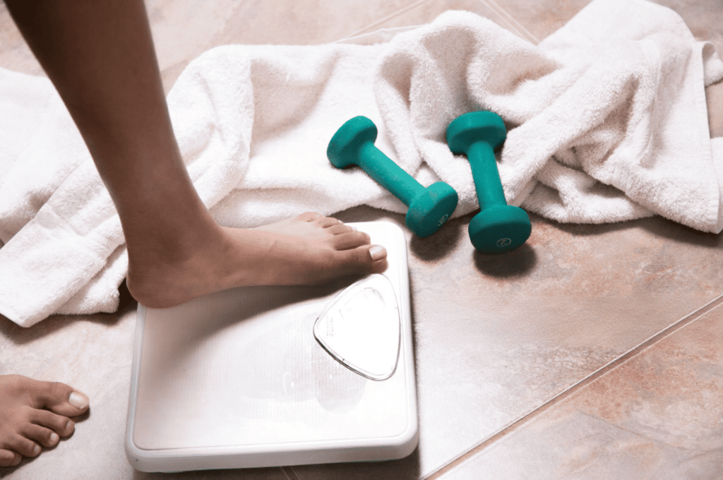 A person is checking their weight after working out with dumbbells.